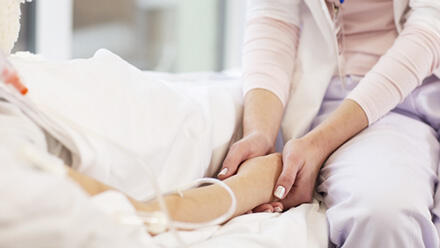 ベッドで点滴を受ける子どもの手を握る大人