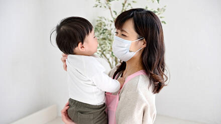 子どもを抱くマスクの保育士