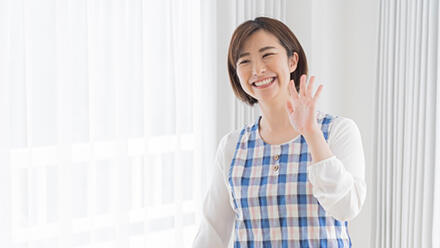 笑顔で手を振るエプロン姿の女性