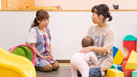 つかまり立ちを見守る保育士